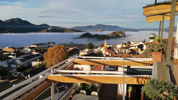 A terrace with outdoor seating, overlooking a coastal town with buildings and mountains in the distance. - Balcon del Velillos - Rincón de Marcelo (Moclin)