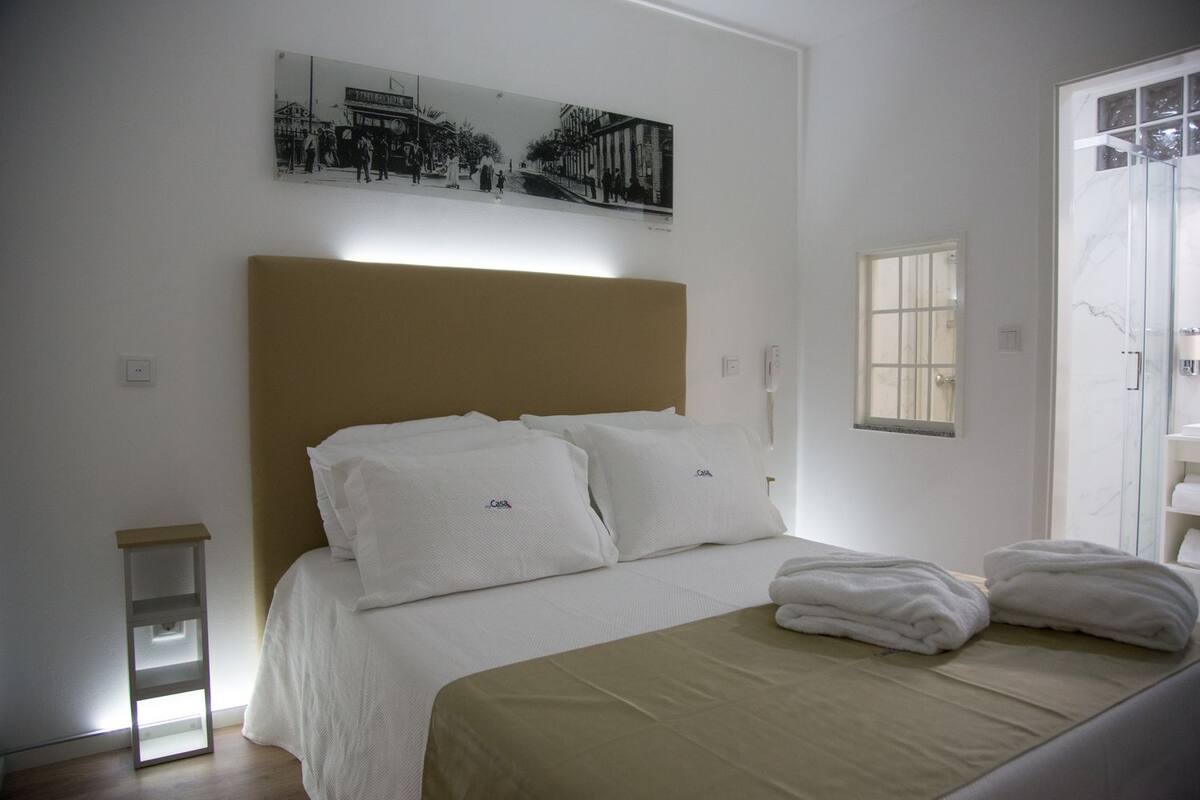 Una habitación de hotel con una cama, una mesita de noche, una ventana y un cuadro en la pared.