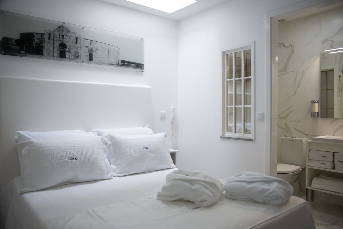 Una habitación de hotel con cama, baño y un ventanal grande.