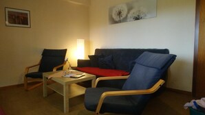 Een zithoek met een bank, twee fauteuils, een bijzettafeltje en een lamp.