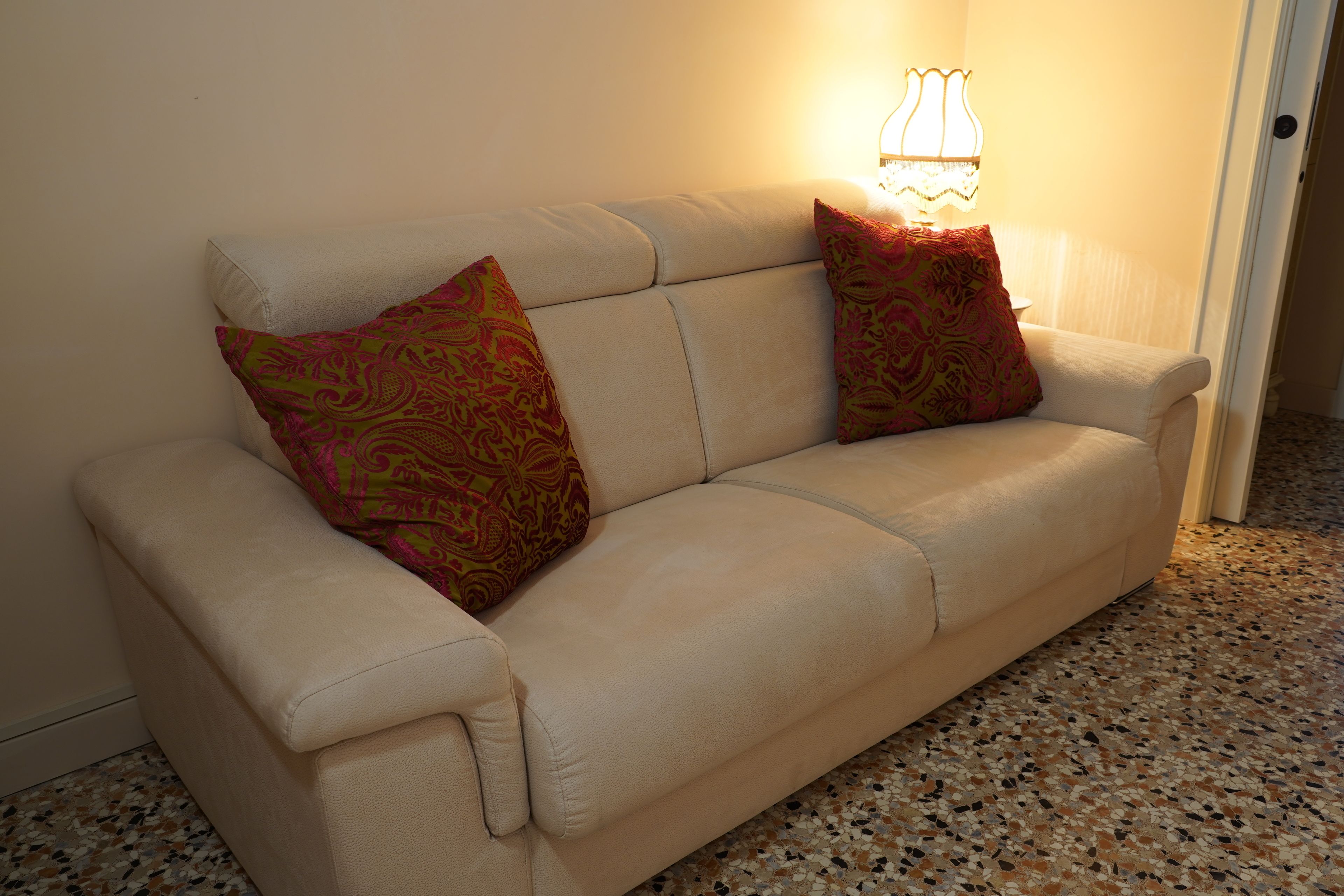 A beige sofa with two patterned cushions and a wall-mounted lamp.