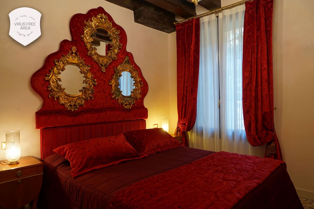 A room with a large bed, ornate gold-framed mirrors, red curtains, and a sign indicating a virus-free area.
