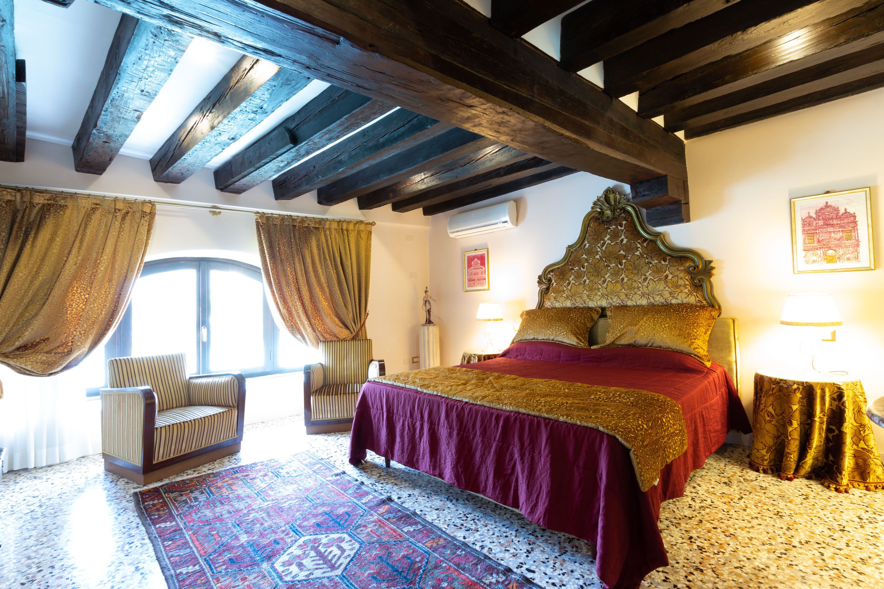 A bedroom with a large bed, a chair, a patterned rug, and a wooden ceiling.