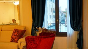 A living room with a sofa, a red armchair, and a window with curtains. - Granda Sweet Suites (Venice)