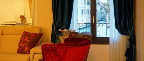 A living room with a sofa, a red armchair, and a window with curtains.