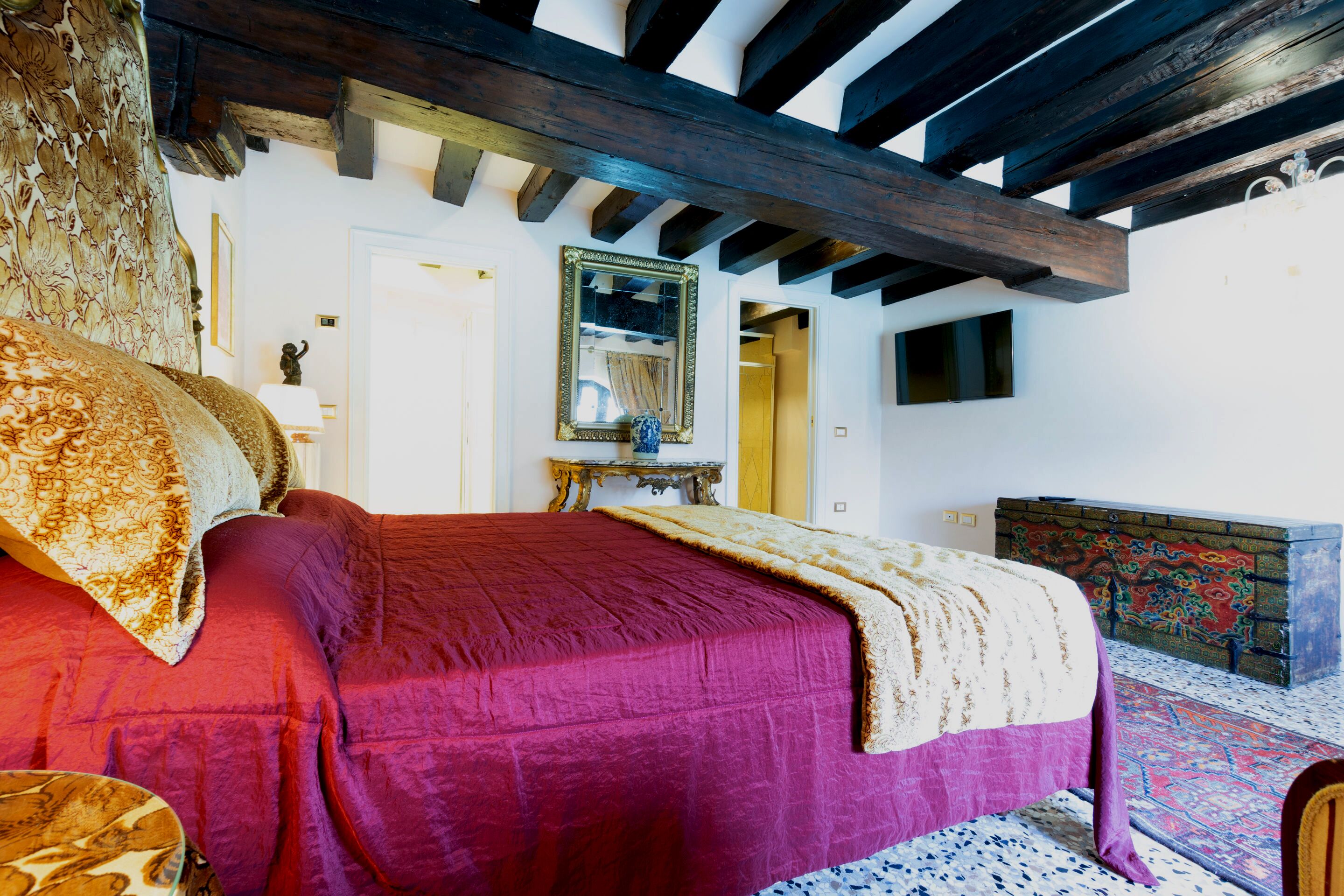 Una habitación con cama, techo de madera, espejo y alfombra estampada.