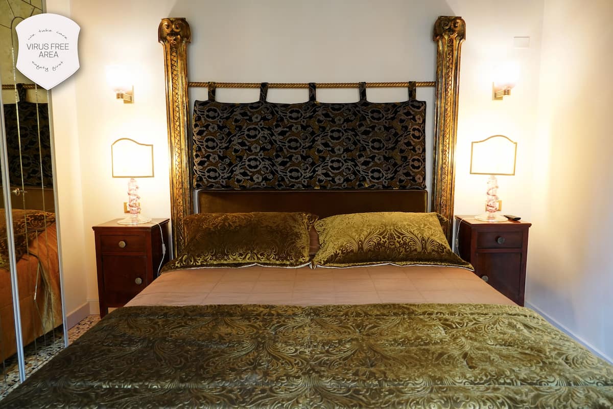 A hotel room with a large bed, ornate headboard, two bedside tables with lamps, and a mirror on one wall.