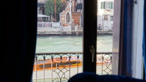 A view from a window overlooking a canal with a boat, buildings, and a fence. - Granda Sweet Suites (Venice)