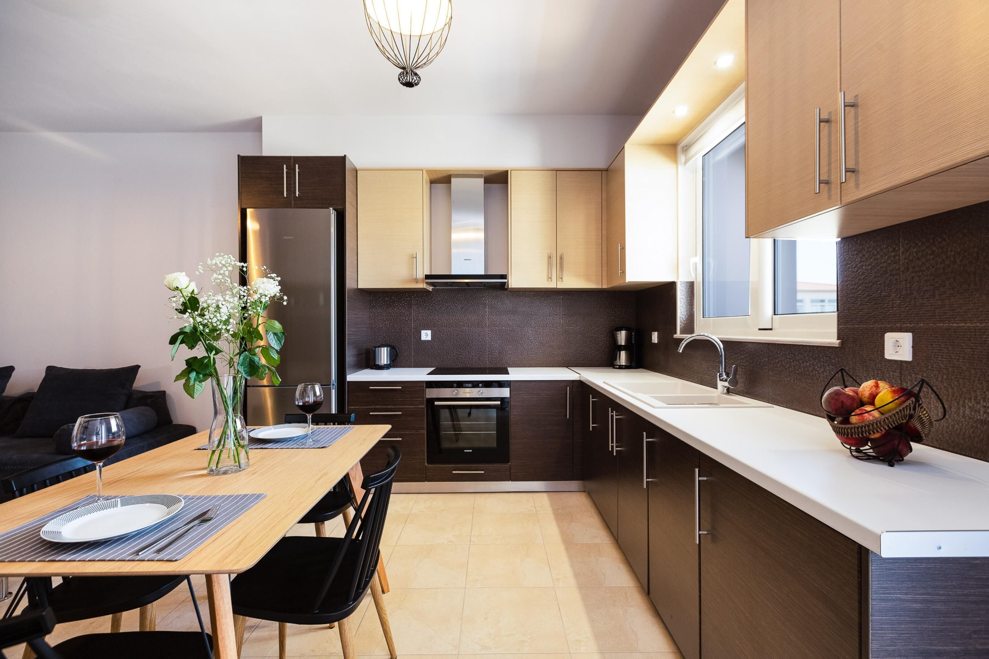 Une cuisine moderne avec des meubles de rangement en bois foncé, un réfrigérateur en acier inoxydable et un plan de travail blanc.