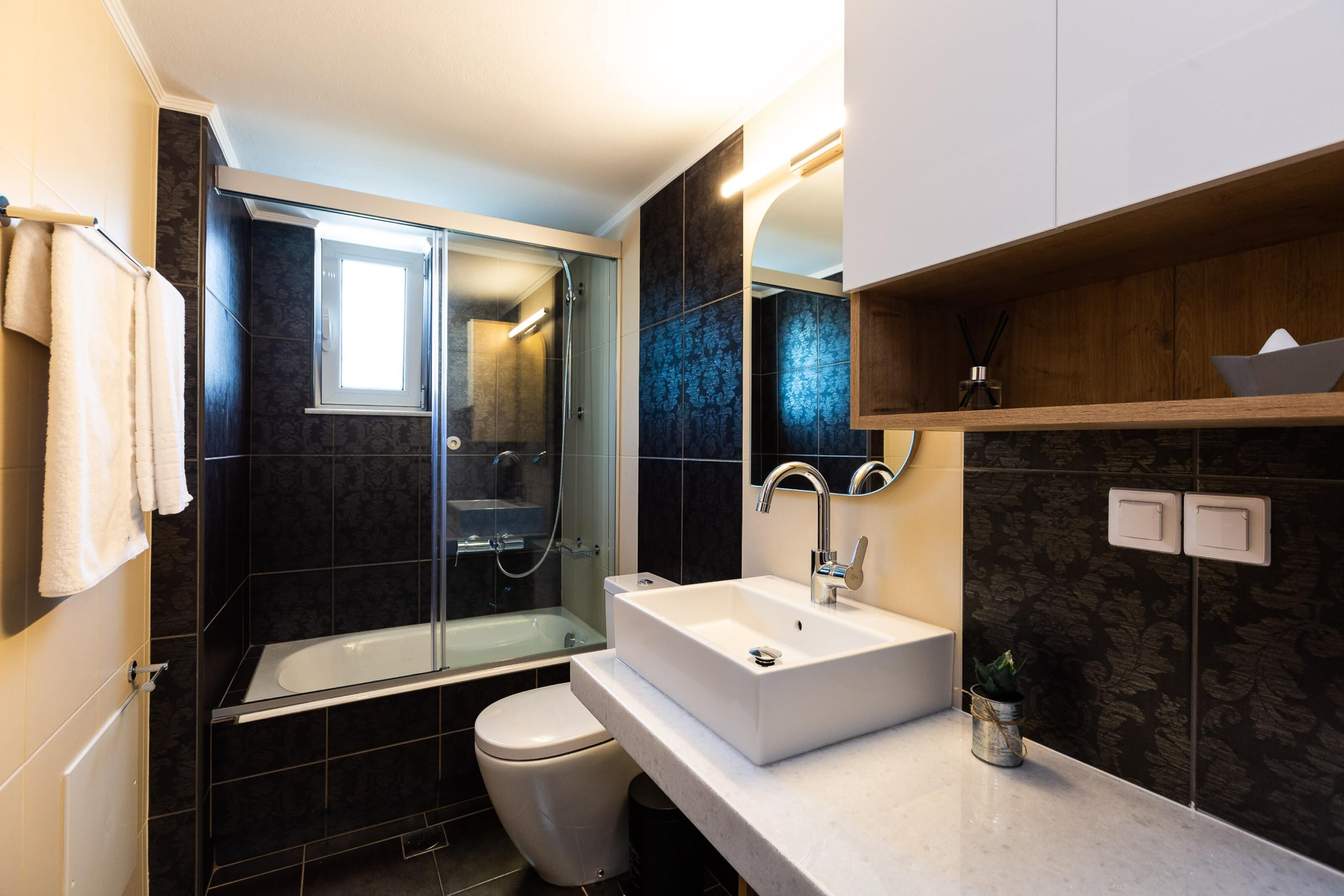 Un baño moderno con ducha de vidrio, lavamanos blanco y retrete.
