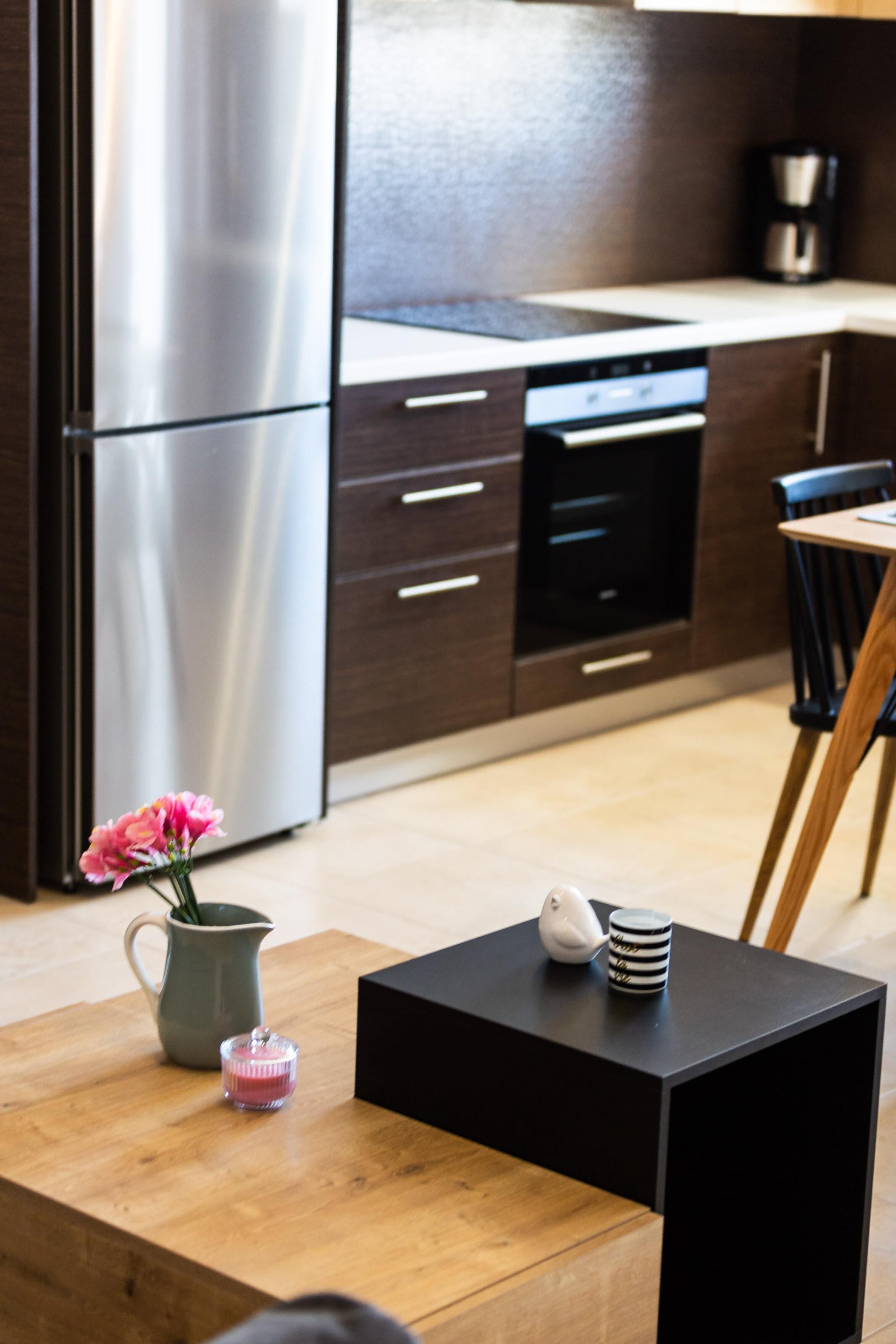 Una cucina moderna con elettrodomestici in acciaio inossidabile, un tavolo in legno con un vaso di fiori e un tavolino nero con una tazza e una candela.