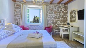 Ein Schlafzimmer mit Steinwand, einem Bett mit weißer Bettwäsche, einem Schreibtisch mit Stuhl und einem Fenster mit Blick auf Bäume.
