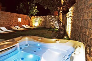 Een hottub met een stenen muur en lounge stoelen op de achtergrond.