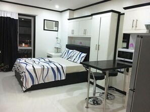 A compact hotel room with a bed, a desk, a chair, a wardrobe, and a television.