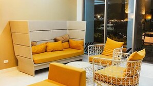 Una sala de estar moderna con un sofá y dos sillones, un ventanal con vista a la ciudad y piso blanco.