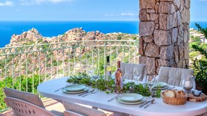 A table set for dining with a view of the sea and rocky terrain.