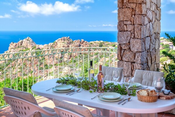 A table set for dining with a view of the sea and rocky terrain.