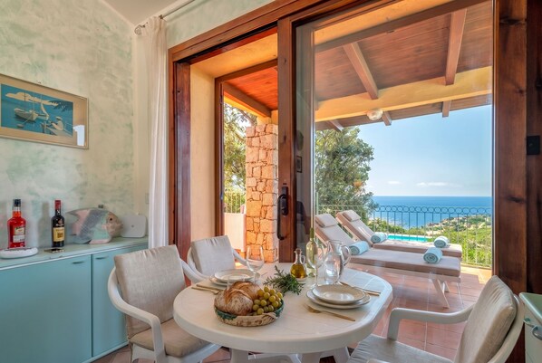 A dining area with a table set for two, a stone pillar, and a view of the sea.