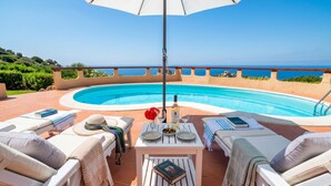 A poolside area with lounge chairs, a table with a book, a bottle, and glasses.