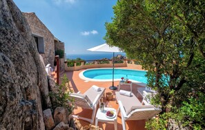 A poolside area with lounge chairs, a table with drinks, and a view of the ocean.