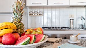 A kitchen with a fruit bowl containing bananas, pineapple, watermelon, and grapes.