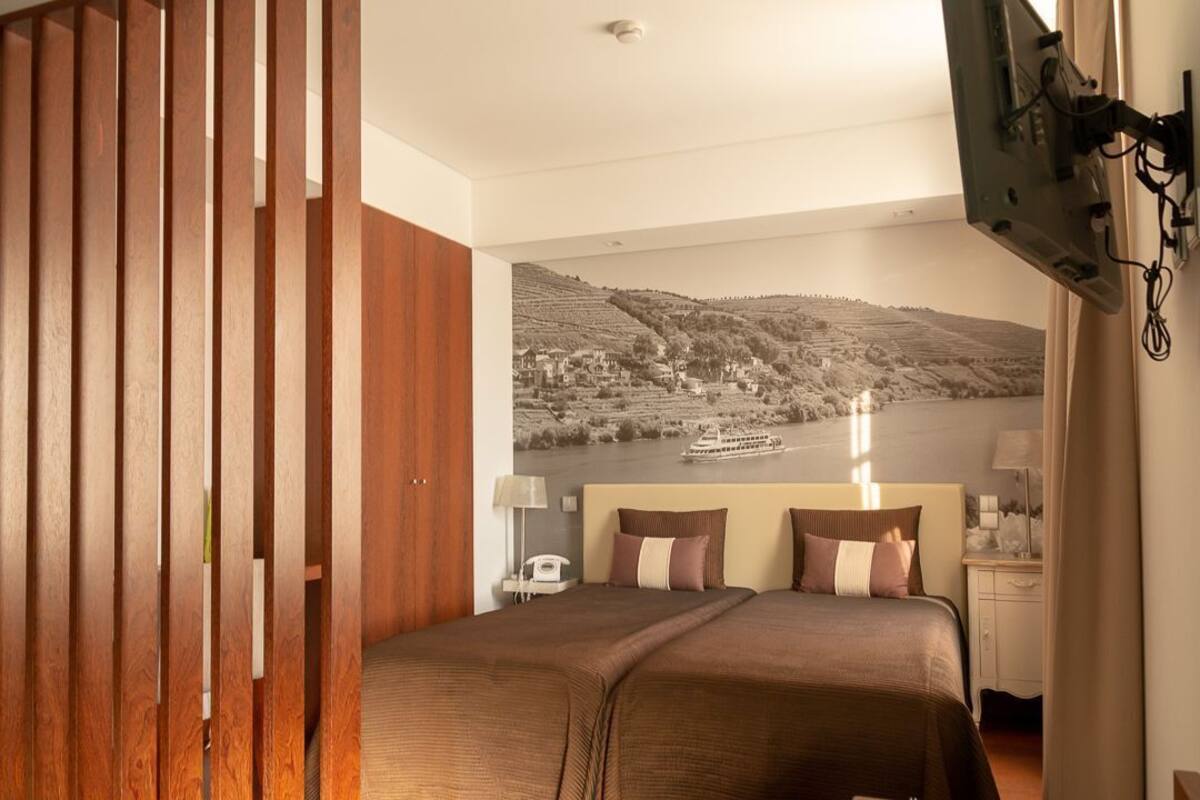 A hotel room with a bed, a nightstand, a lamp, a telephone, and a wall-mounted TV.