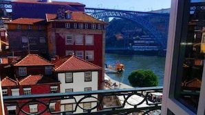 A balcony with wrought iron railings overlooking a river, buildings with red-tiled roofs, and a bridge in the background. - Oca Ribeira do Porto Hotel (Porto)