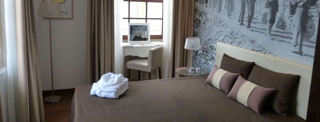 Una camera d'albergo con un letto, una scrivania, una sedia, una lampada e un quadro appeso al muro.