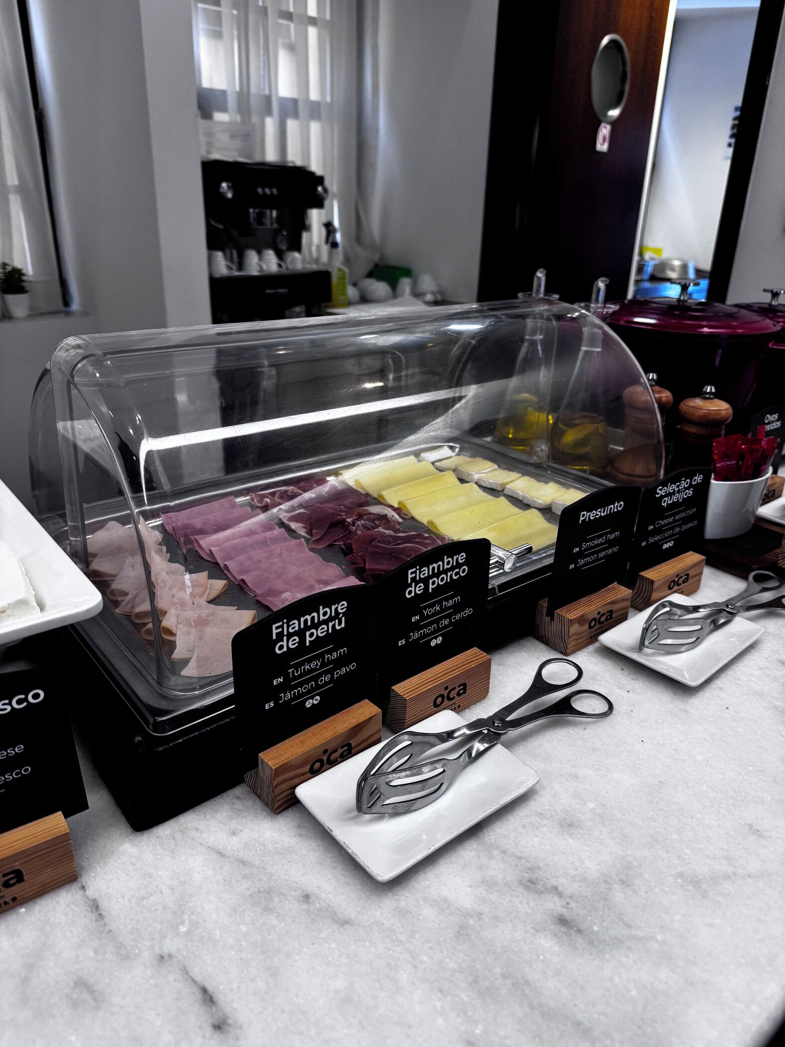 Mostrador de delicatessen con diversos embutidos y quesos, incluyendo jamón de pavo y jamón ahumado, expuestos en una vitrina.