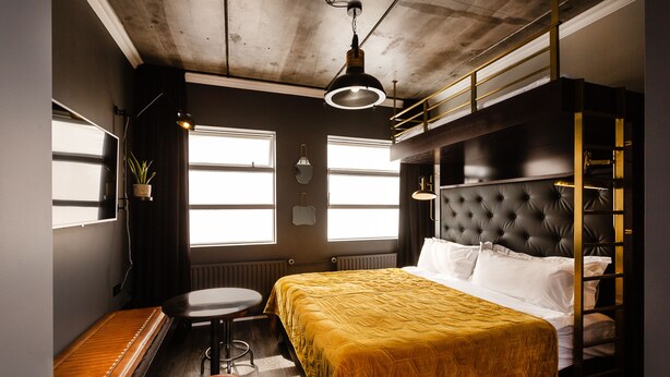 A compact hotel room with a bunk bed, a small desk, a chair, and a window providing natural light. - Urban Reykjavik Studios (Reykjavik)