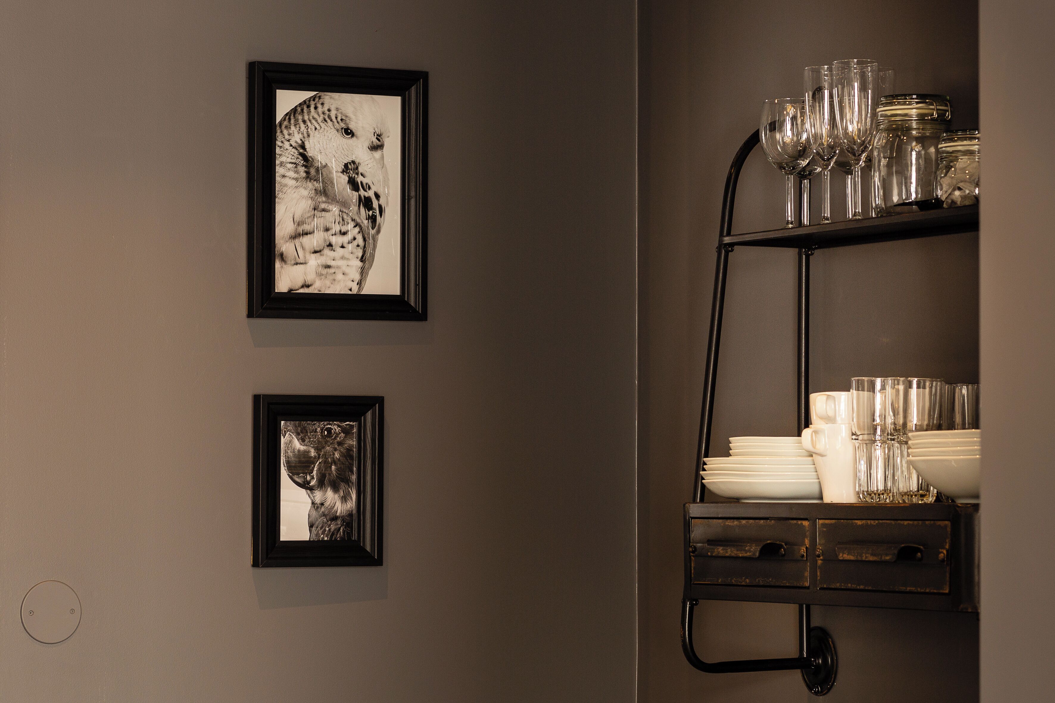 A wall with two framed photographs and a metal shelf with glassware and dishes.
