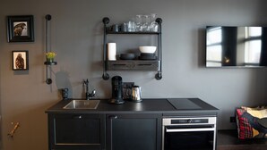 A modern kitchen with a built-in oven, a coffee maker, and a shelf with glassware and dishes. - Urban Reykjavik Studios (Reykjavik)
