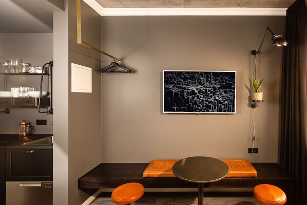 Una cocina moderna con horno integrado, un comedor con mesa redonda y asientos color naranja, y una planta suspendida en la pared.