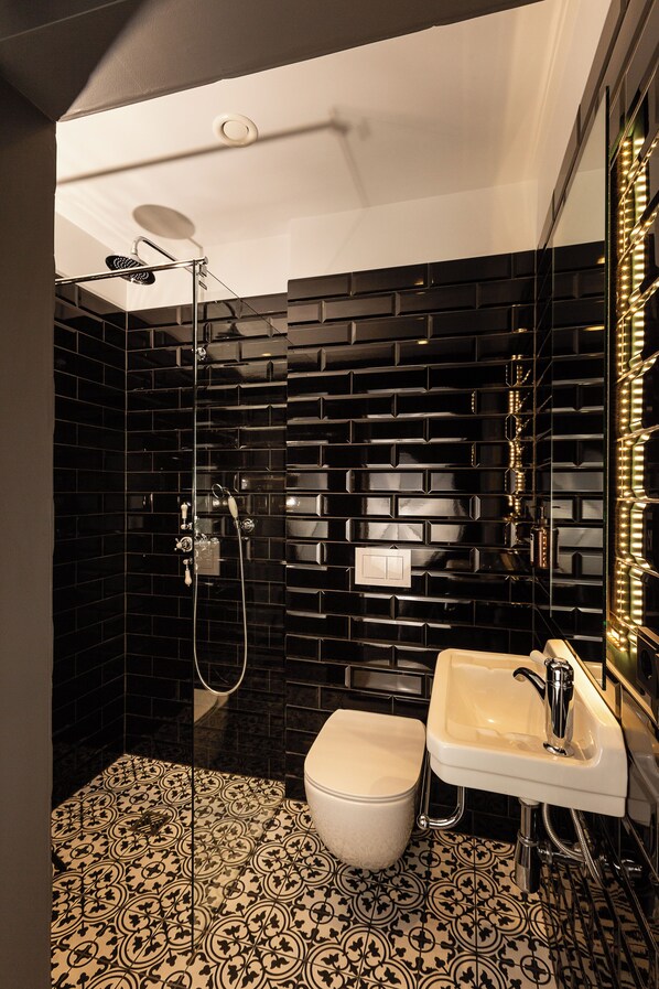 Un baño con pared de azulejos negros, inodoro blanco y lavamanos con espejo.