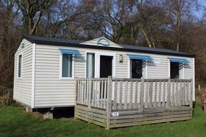 A small, single-story mobile home with a front porch and a number '53' sign.
