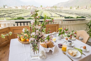 Une table dressée avec des aliments pour le petit-déjeuner, un vase rempli de fleurs et une vue pittoresque sur un vignoble.