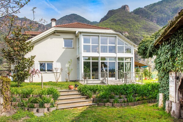 A house with a garden, steps leading to the entrance, and a mountain backdrop.
