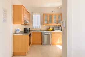 A compact kitchen with wooden cabinets, a dishwasher, a microwave, and a fruit bowl.