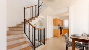 A staircase with a wooden handrail and black balusters, leading to a kitchen area with wooden cabinets and a dining table set with plates and glasses. - Beautiful holiday house with Heated Pool, Private Patio and Great Location (Puerto del Carmen)