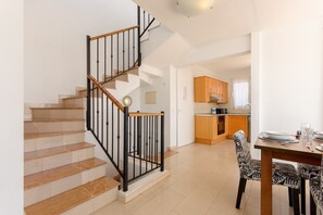 A staircase with a wooden handrail and black balusters, leading to a kitchen area with wooden cabinets and a dining table set with plates and glasses.