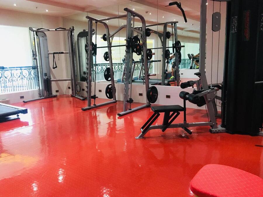 Ett gym med olika typer av träningsredskap, ett rött golv och ett fönster med utsikt.