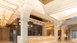 A spacious lobby with a reception desk, large columns, and a chandelier. - The Monarch Hotel (Calasiao)