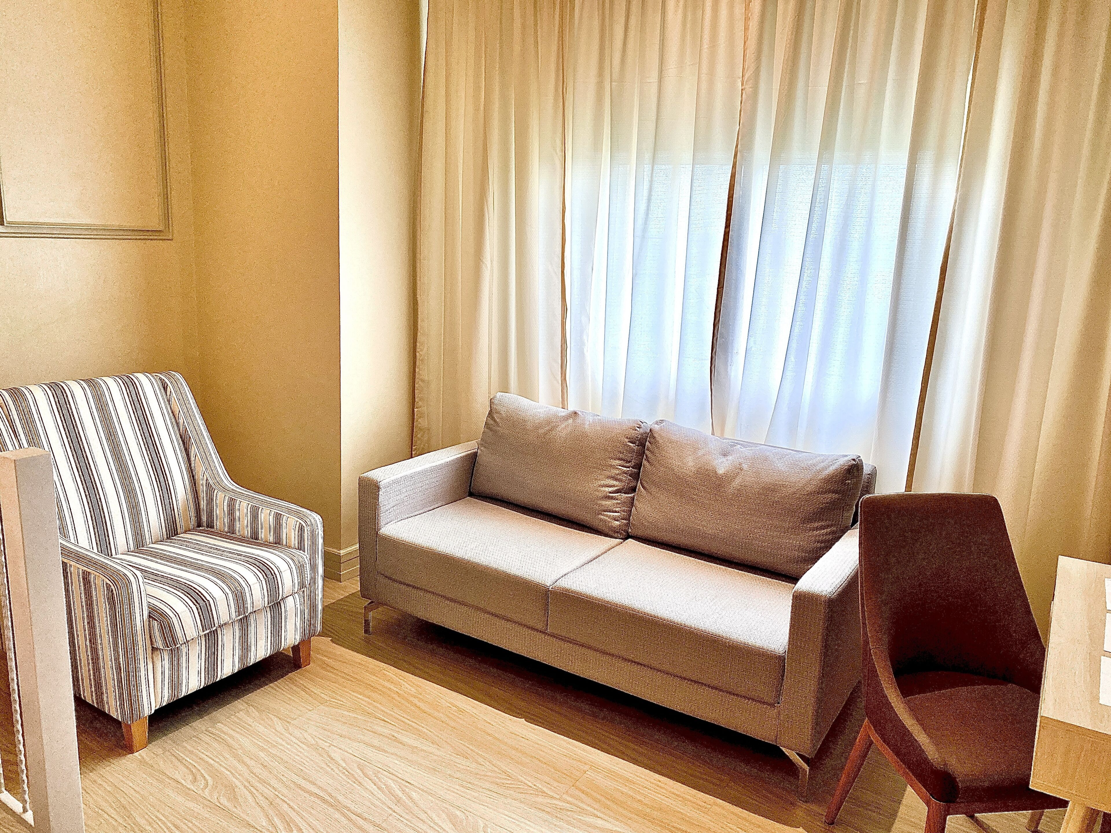 Ein Wohnzimmer mit einem gestreiften Sofa, einem schlichten Sofa und einem Holzstuhl.