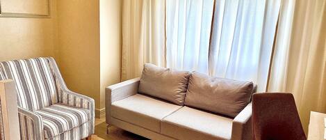 Una sala de estar con un sofá a rayas, un sofá sencillo y una silla de madera.