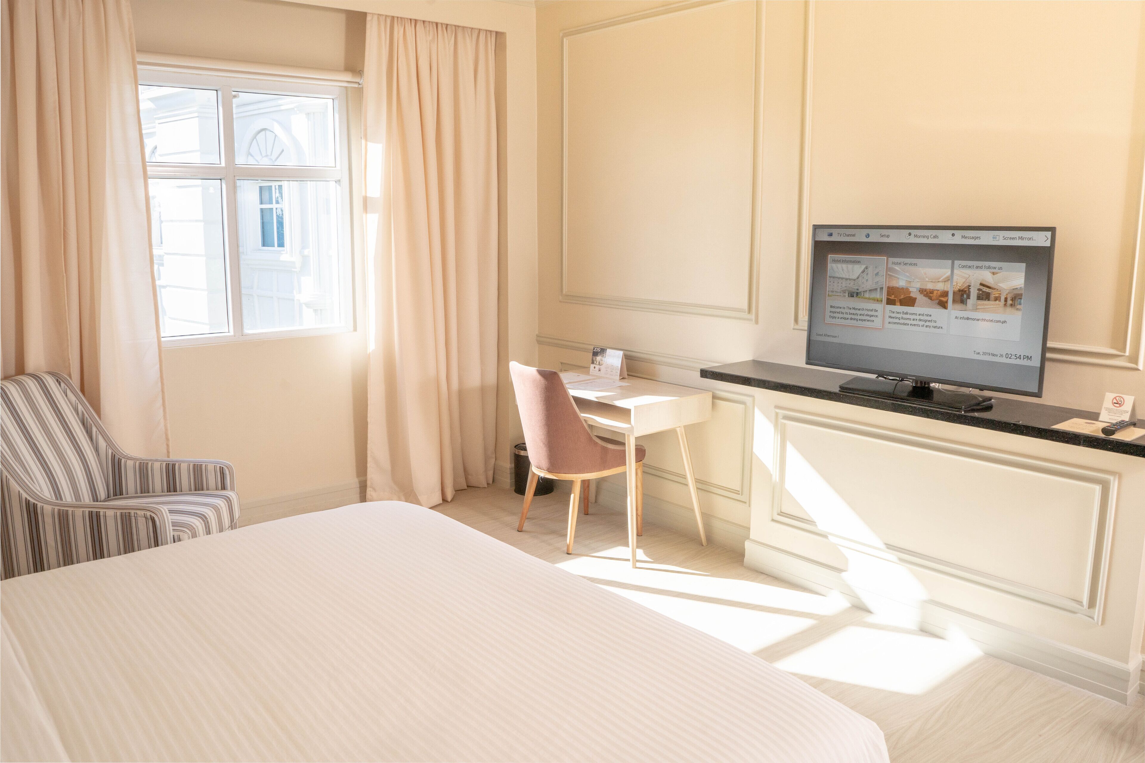 A hotel room with a large bed, a desk with a chair, a television, and a window with curtains.