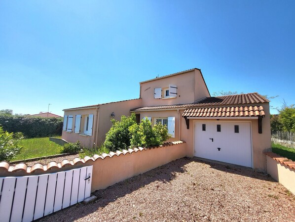 A two-story house with a tiled roof, a garage, and a gravel driveway.