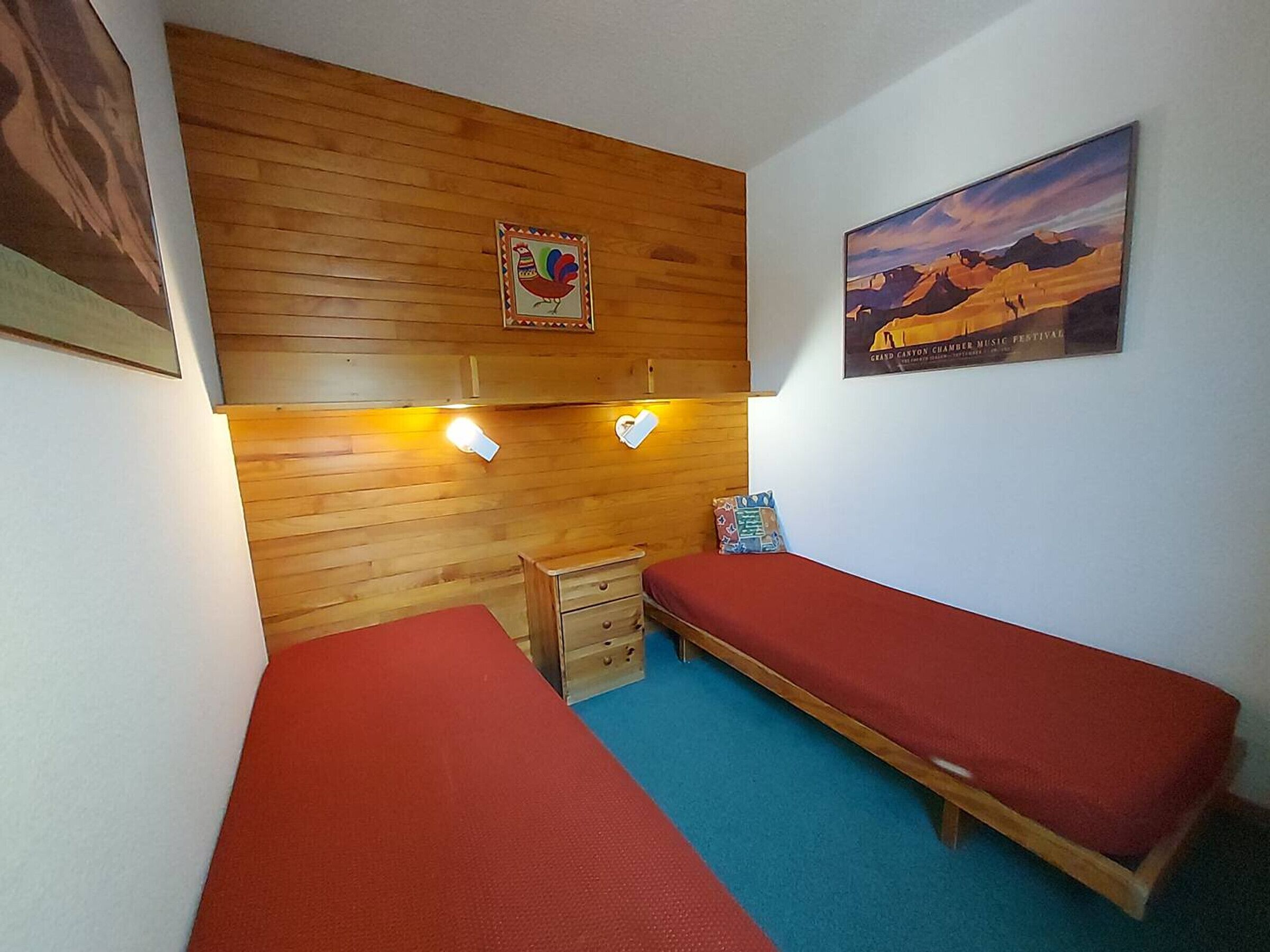 A small room with two single beds, wooden paneling on the walls, a small wooden chest, and two wall-mounted lights.