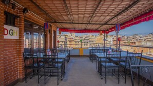 Un patio al aire libre con mesas y sillas, un muro de ladrillo con un letrero, y edificios a la vista al fondo.