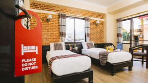 Habitación de hotel con dos camas, una pared de ladrillo, una ventana con cortinas y un balcón.