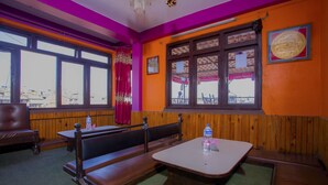 Un restaurante con bancos y mesas de madera, ventanas amplias con cortinas y vistas al exterior.